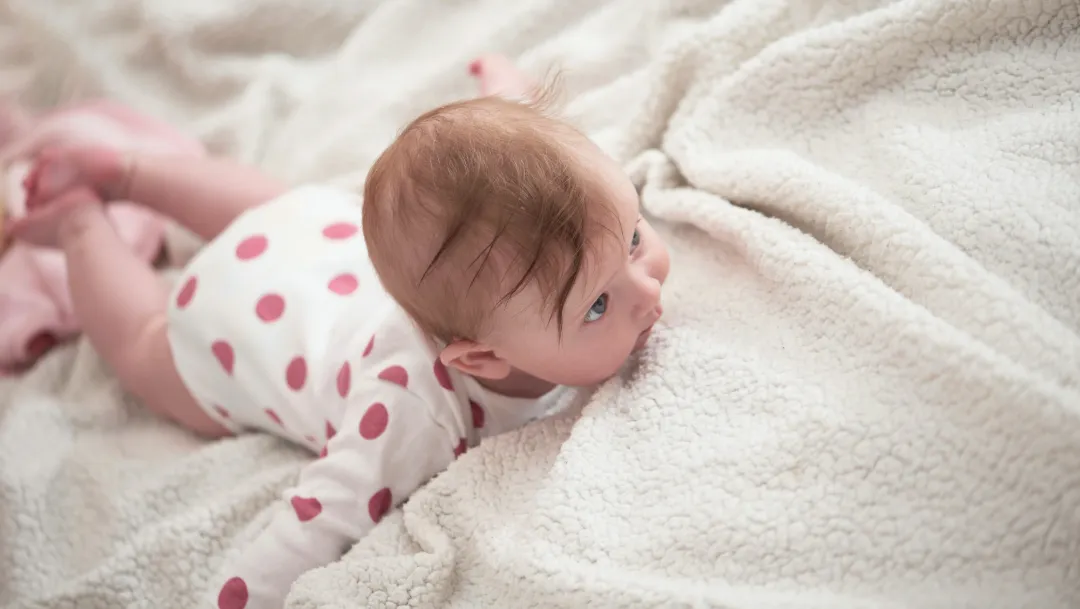 Un bébé allongé sur le ventre sur une couverture blanche douce